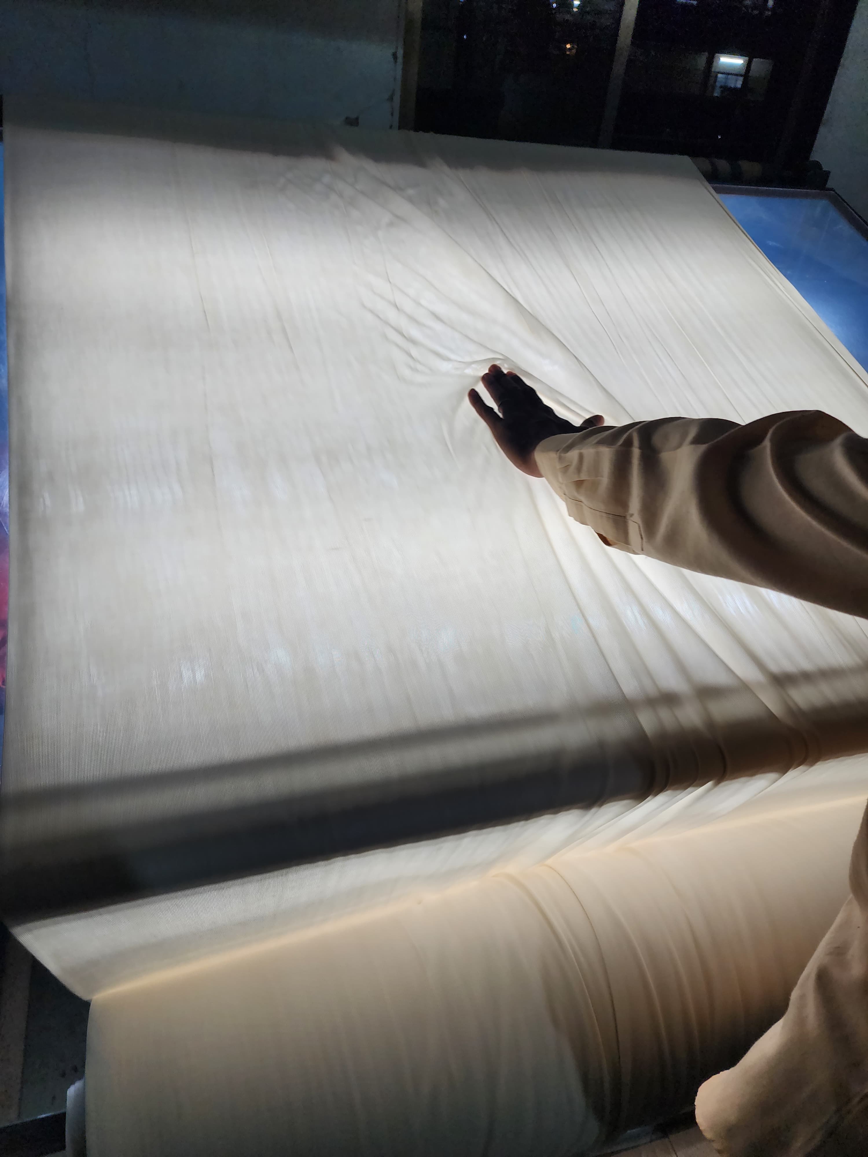Quality inspector manually checking Supima cotton fabric on a backlit inspection table for knitting defects