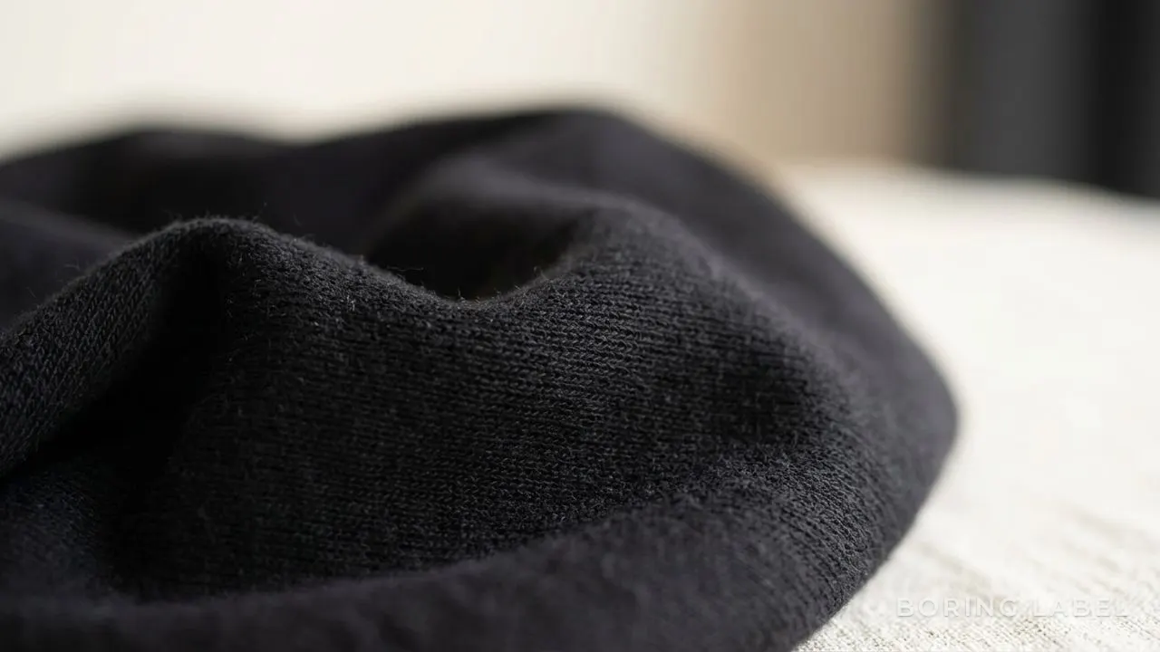 Macro detail of deep black cotton jersey knit, soft raking light revealing fine fabric texture, monochrome still life, calm and minimal, no text or branding
